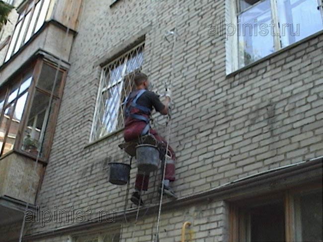 промышленный альпинист проводит монтаж водосточных ухватов по водосточному стояку на фасаде здания