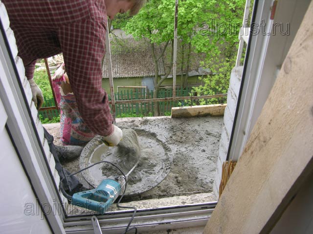 специалист компании замешивает бетонный раствор для устройства новой стяжки на полу плиты балкона