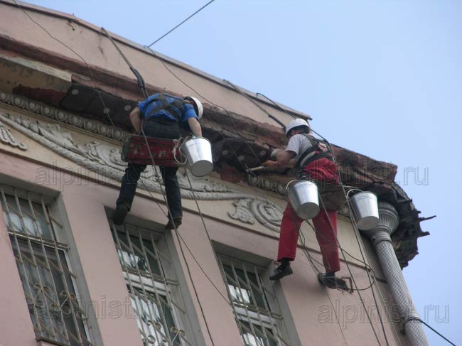 альпинисты крепят металлическую сетку, сложенную в несколько слоев, перед оштукатуриванием карниза здания