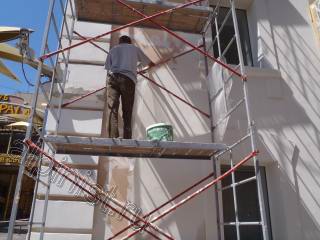 Наш специалист в данный момент проводит фасадные работы, а именно крепит стекловолокнистую сетку «Строби» на поверхность фасада и шпаклюет по ней фасадной шпаклевкой, откосы и архитектурные элементы мы также шпатлюем по сетке.