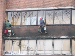 На данной фотографии показаны наши альпинисты, которые моют окна балкона и  очищают кирпичное здание специальным средством для очисти фасада после пожаров.