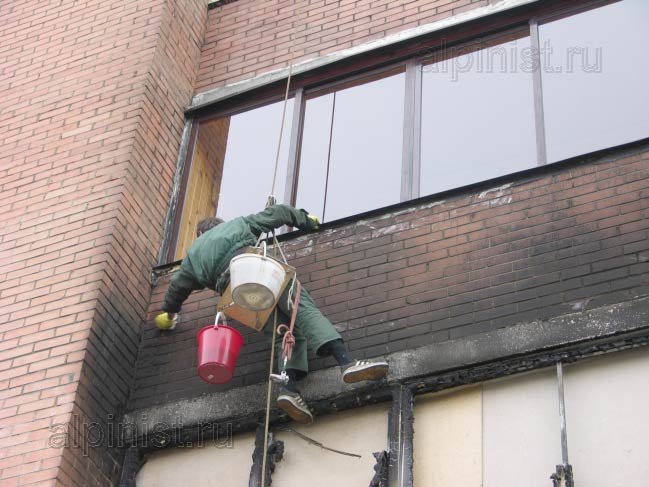 альпинист смывает копоть пожара, с фасада жилого кирпичного дома