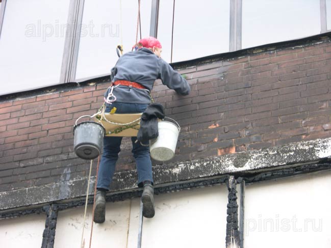 промышленный альпинист наносит на фасад специальный раствор для очистки нагара после пожара