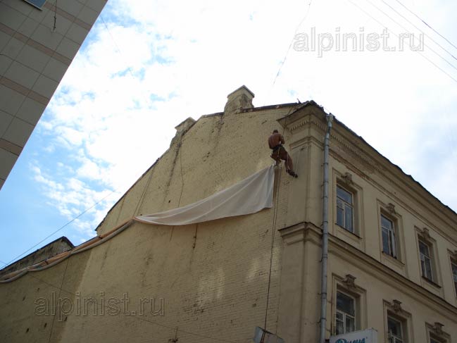 альпинист готовится крепить боковую часть баннера, продевая репшнур через люверсы и кольца дюбелей, прикрученные к стене