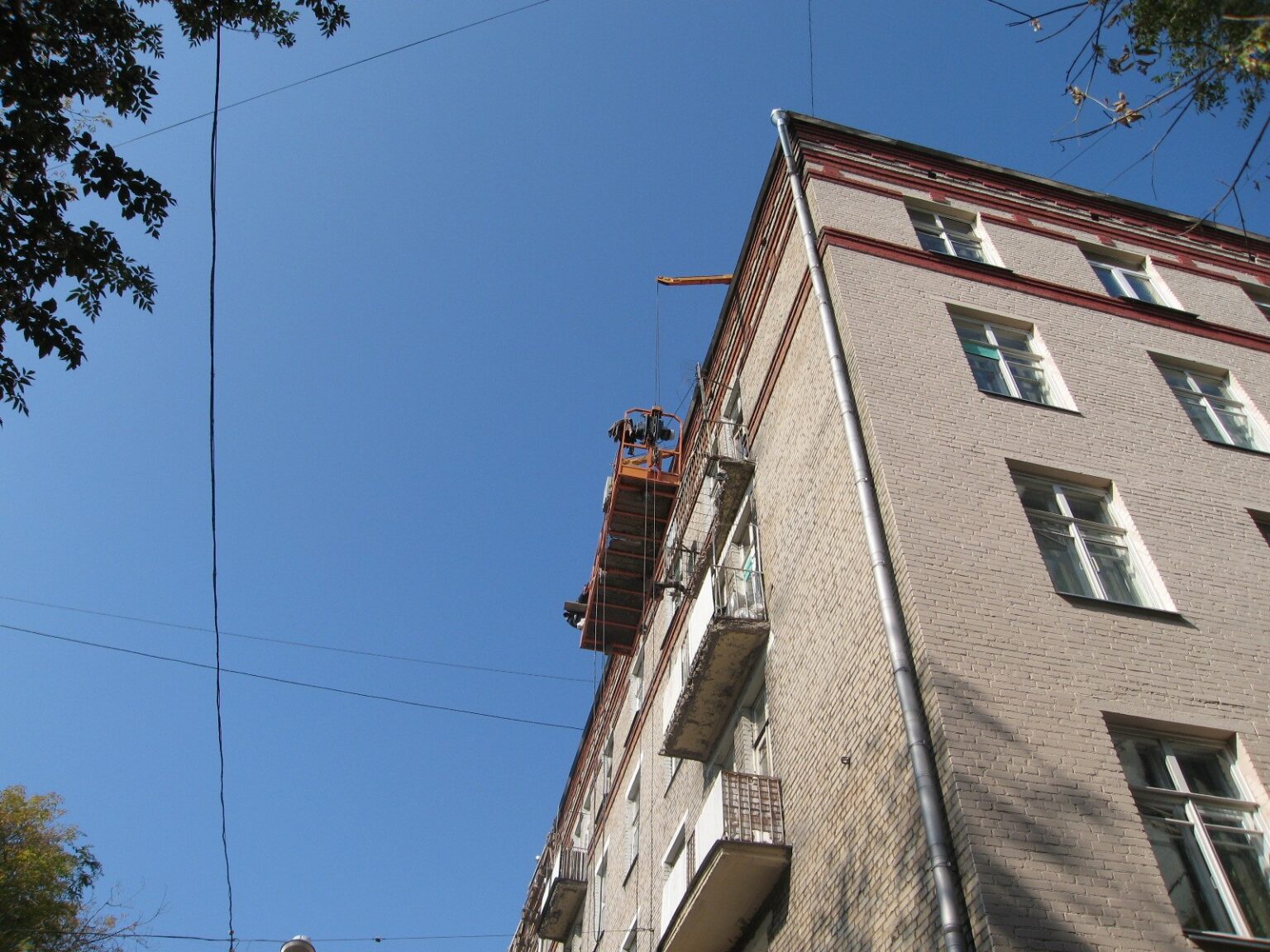 Строительная люлька у угла фасада и водостока во время восстановления балконных плит