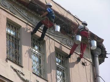 Два промышленных альпиниста крупным планом отбивают старую штукатурку фасада